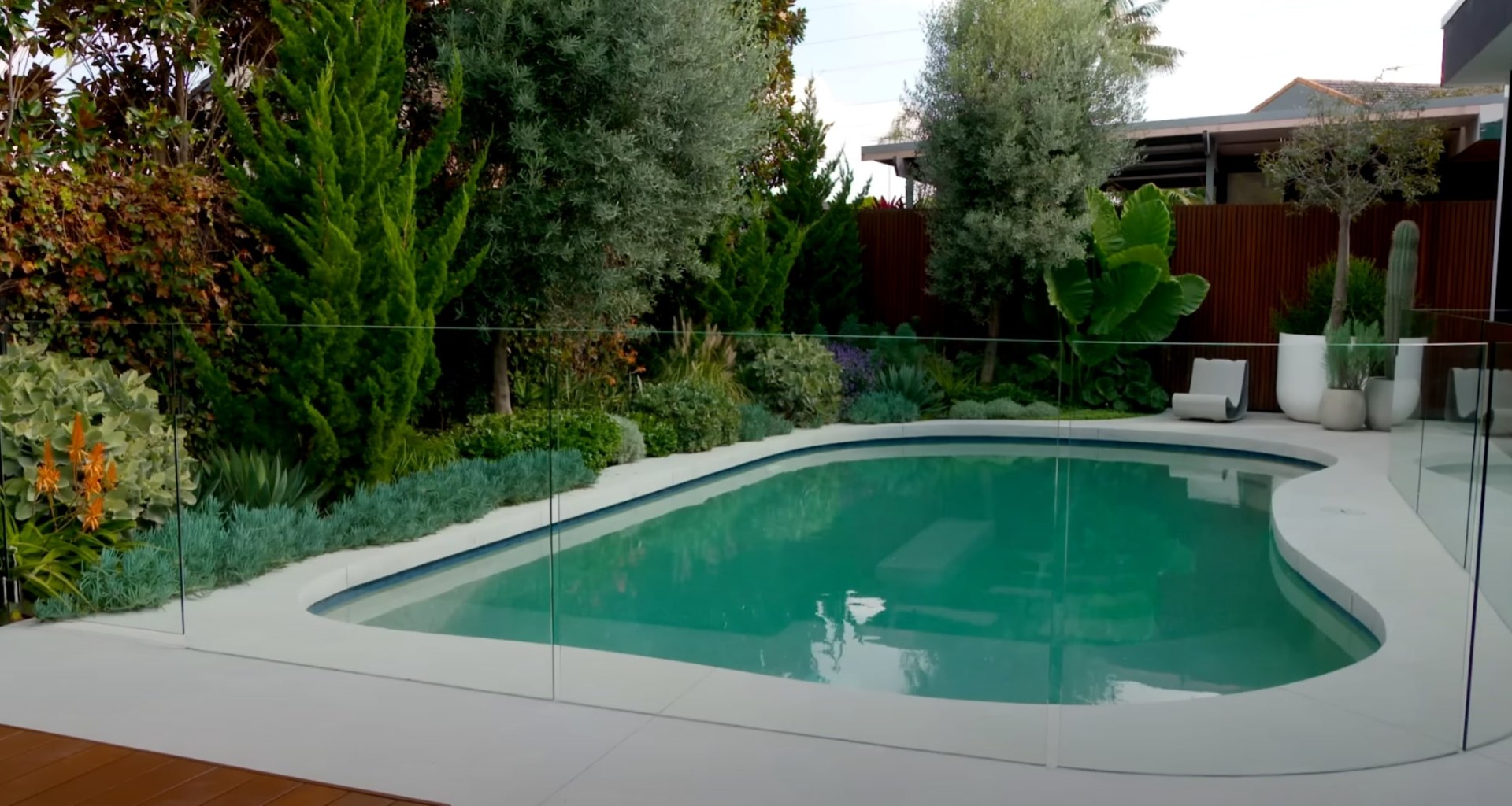Complete Landscape Design - Pool and Garden Integration Modern pool area with professional landscaping and glass safety fencing