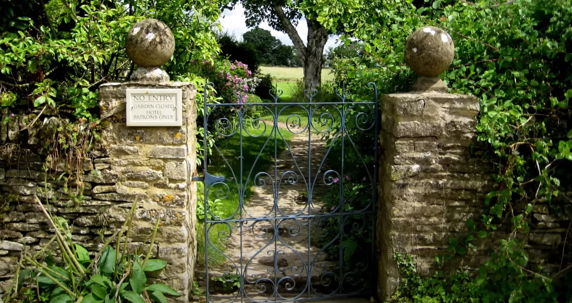Classic Landscape Design - Traditional Garden Elements Traditional stone garden gate with ornate ironwork surrounded by mature landscaping